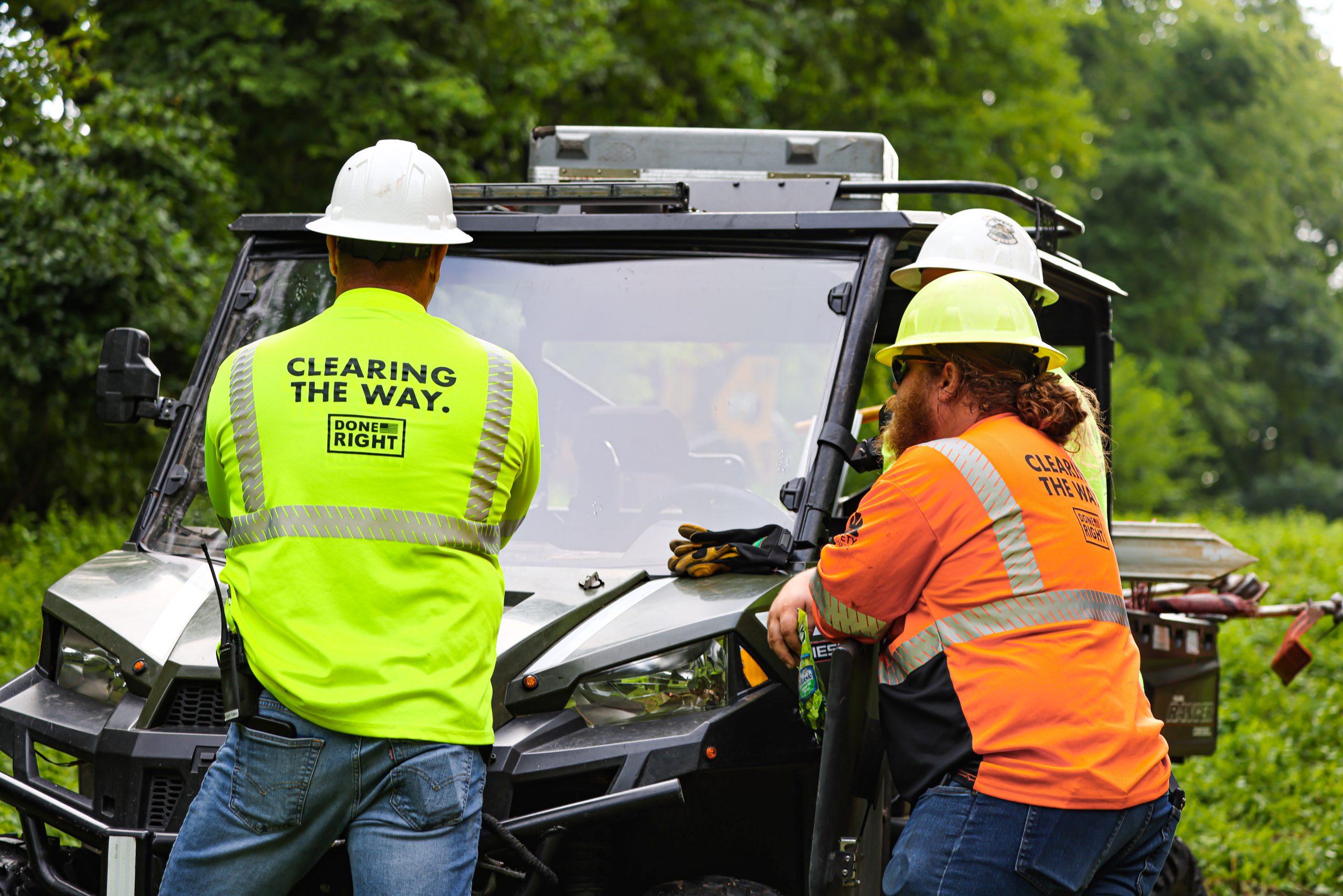 Three Lanracorp employees in hard hats and neon vests standing at a utility vehicle at a work site