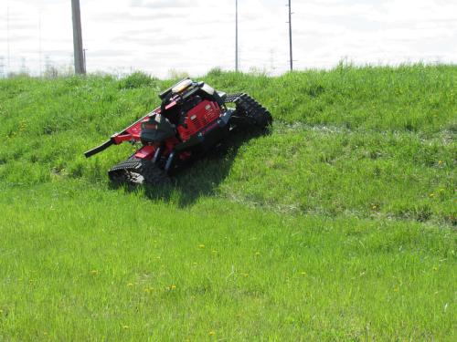 red and black mower mowing grass on an incline
